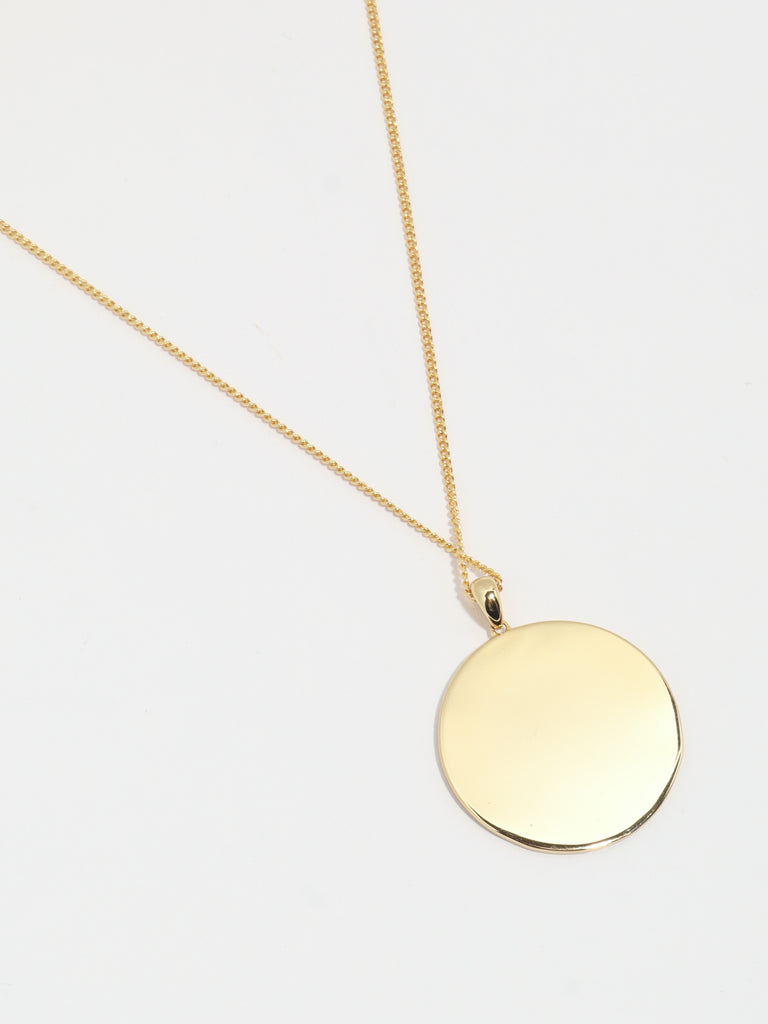 back of gold necklace with circle shaped pendant with House of eleven logo printed in the center