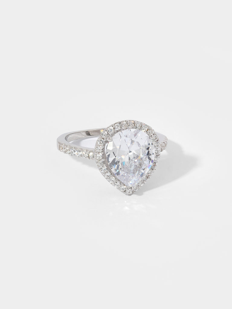 "Image description: A ring featuring a pear-cut center stone surrounded by a pavé set crystal halo. The ring is made of solid .925 sterling silver, is nickel-free, and rhodium plated. The center stone measures 10mm x 12mm in a pear shape, and the ring houses 27 brilliant-cut cubic zirconia stones, each measuring 1mm in diameter."