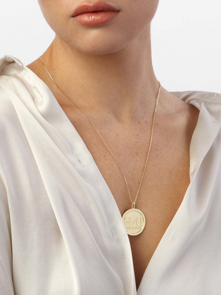 woman wearing gold necklace with circle shaped pendant with House of eleven logo printed in the center
