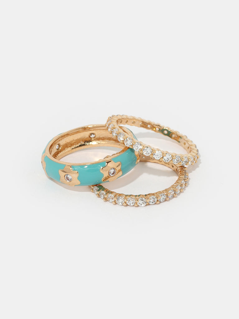 three gold rings; two are identically covered in small clear-colored round crystals. the other band is coated with a turquoise enamel with gold flower shaped motif with a small clear-colored crystal in the center