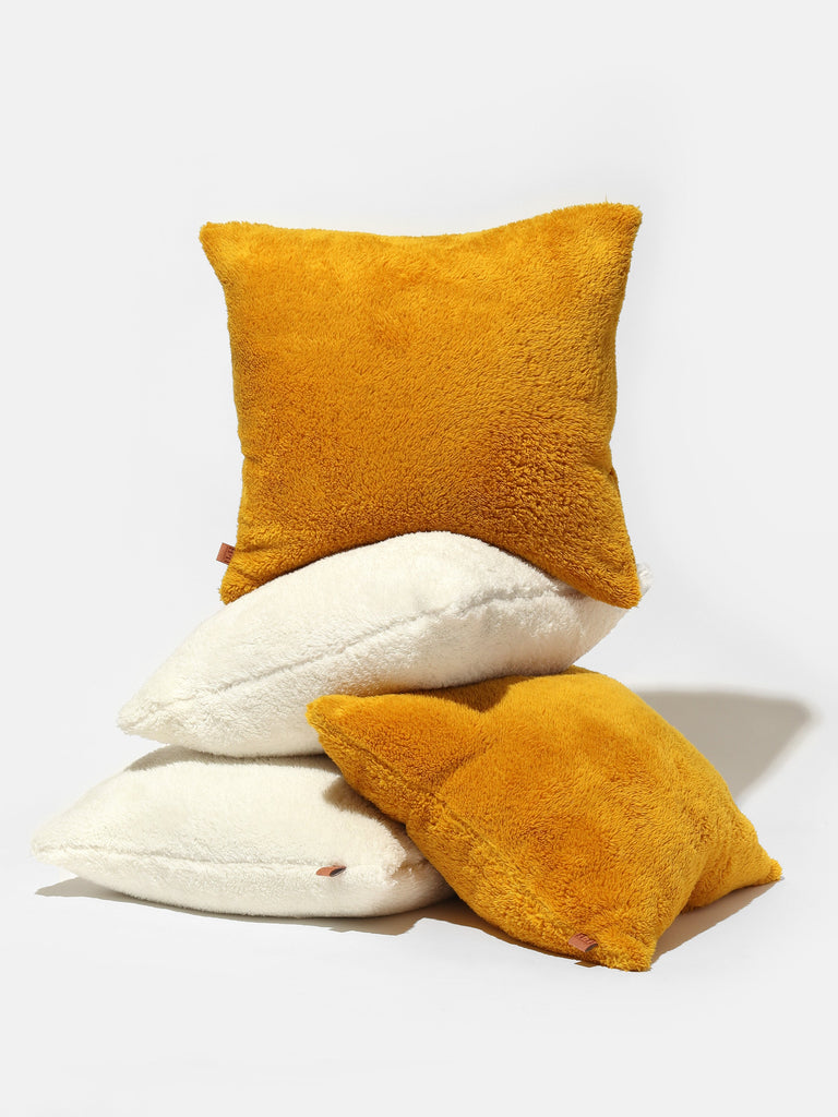 A pile of four pillows, two white and two yellow, against a white backgrouns
