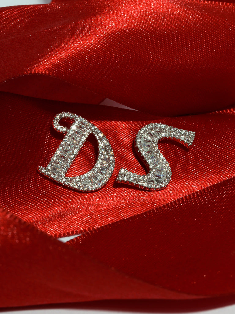 Silver and crystal D and S pins resting agains red ribbon