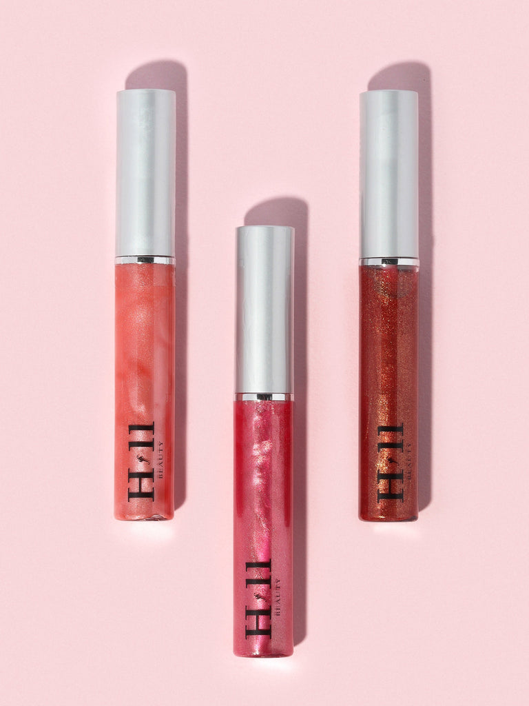Three lip glosses against a pink background