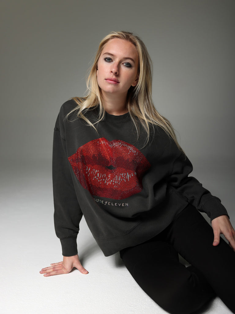 Woman wearing charcoal crewneck sweater with bedazzled kissing lips