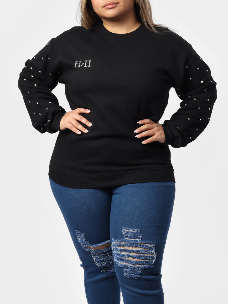 Woman wearing black crewneck sweater with a mini bedazzled HOF11 logo
