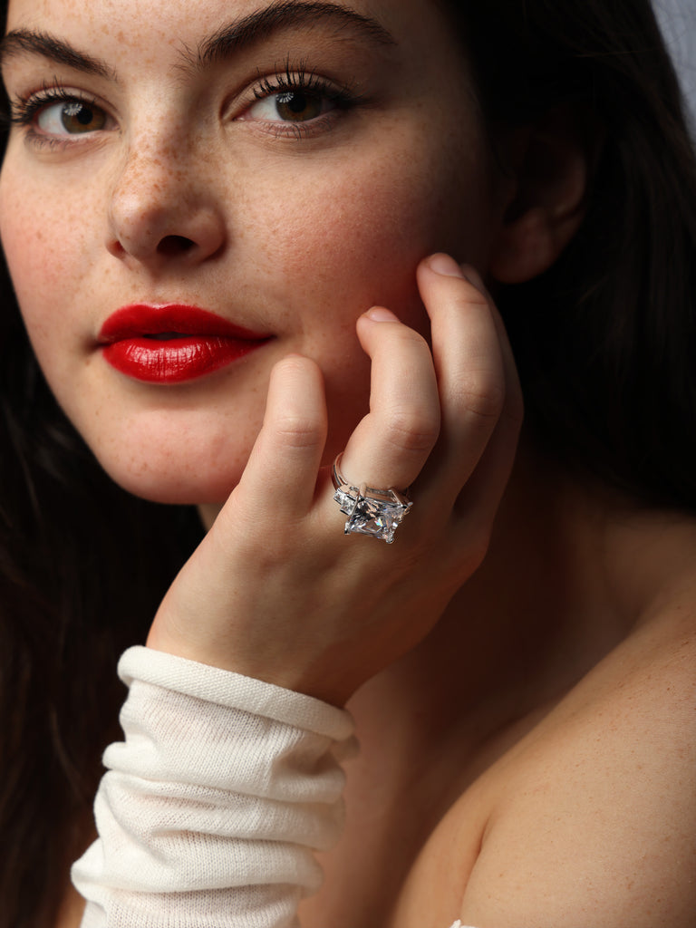 woman wearing silver ring with large square shaped, clear-colored gem in the center and two smaller square shaped gems on each side
