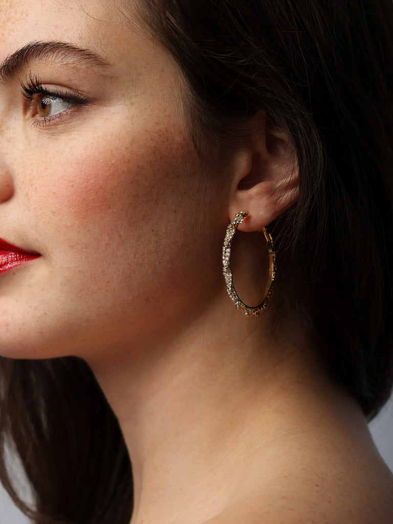 Image of woman wearing gold hoops covered in small clear crystals in criss-cross pattern