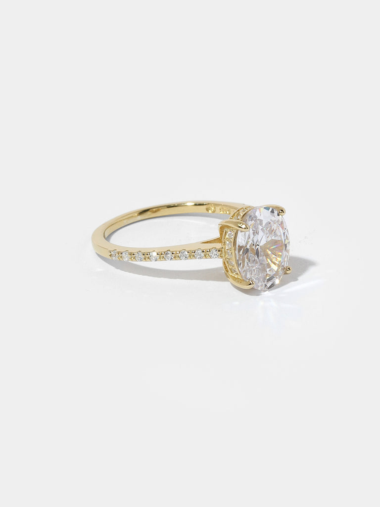 gold ring with large oval shape, clear-colored gem in the center and small clear crystals on the side of the band and prong