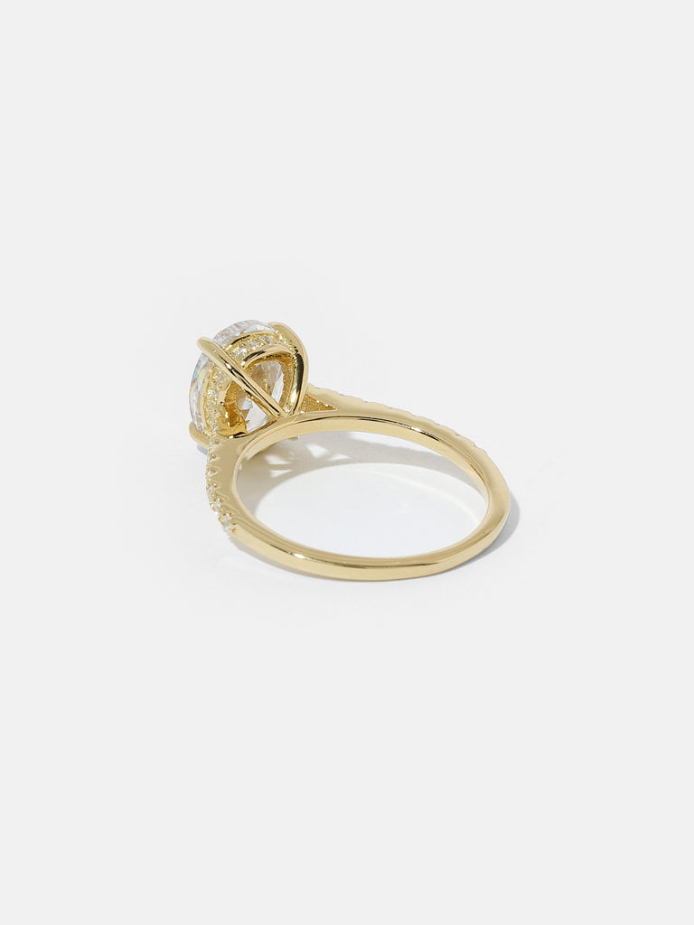 back of gold ring with large oval shape, clear-colored gem in the center and small clear crystals on the side of the band and prong