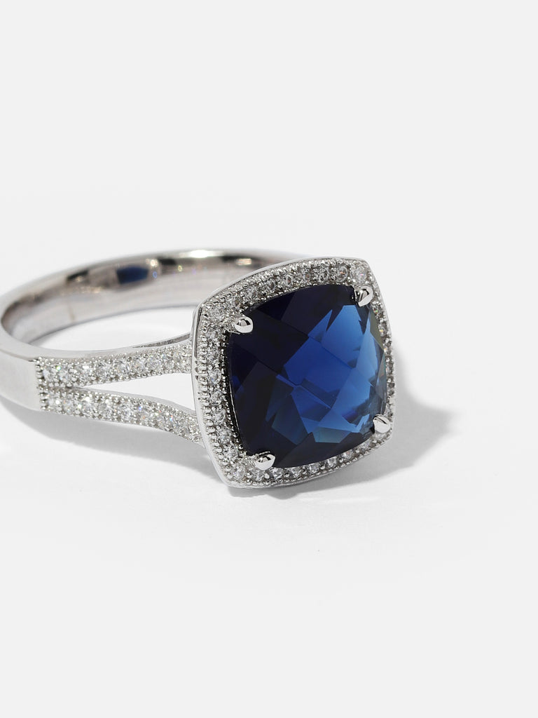 Silver ring with large square shaped blue sapphire colored gem outlined with small clear crystals