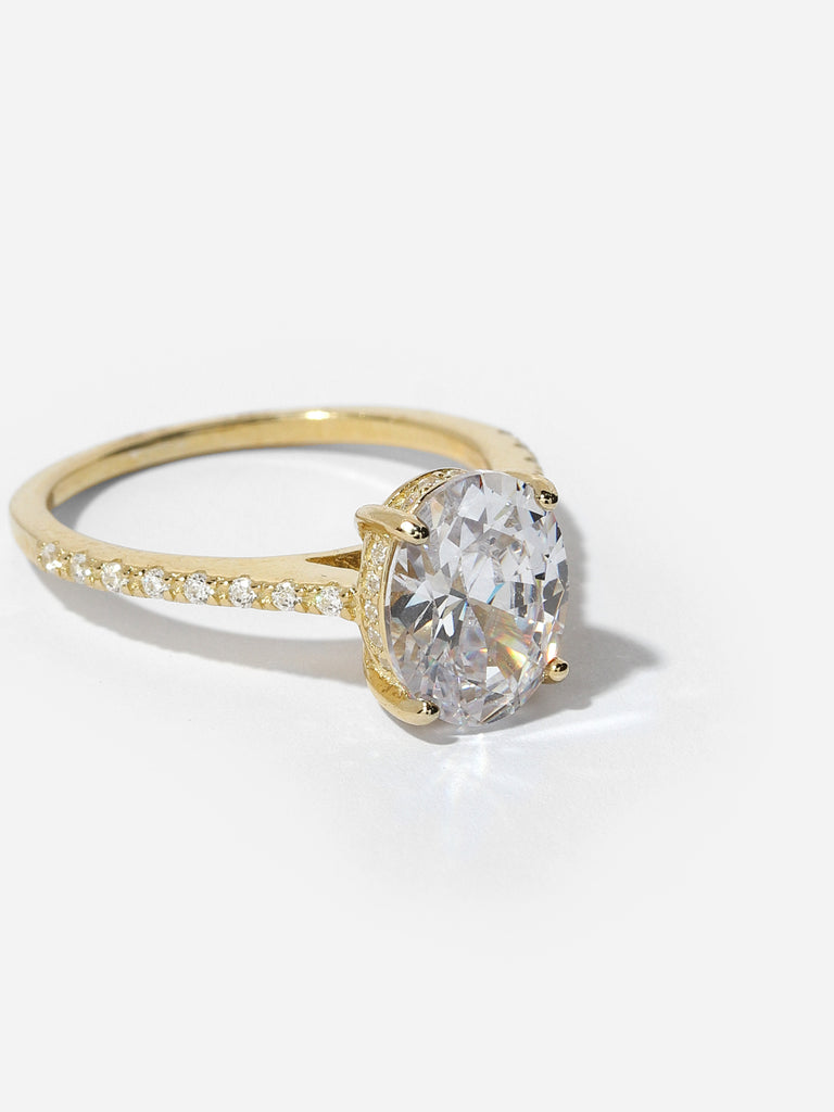 gold ring with large oval shape, clear-colored gem in the center and small clear crystals on the side of the band