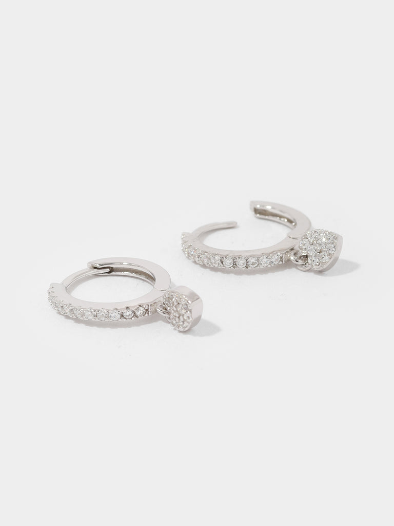 silver hoop earrings covered in small circular, clear-colored crystals and a dangling heart shaped charm covered in clear-colored crystals