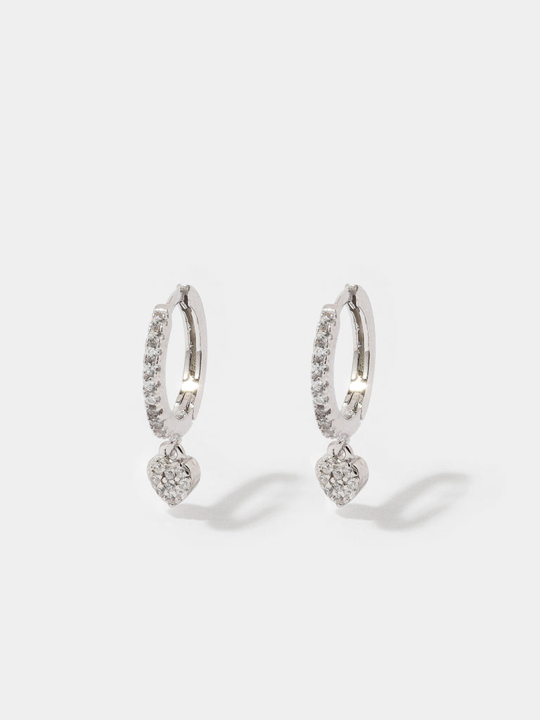 silver hoop earrings covered in small circular, clear-colored crystals and a dangling heart shaped charm covered in clear-colored crystals