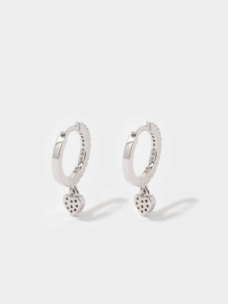back of silver hoop earrings covered in small circular, clear-colored crystals and a dangling heart shaped charm covered in clear-colored crystals