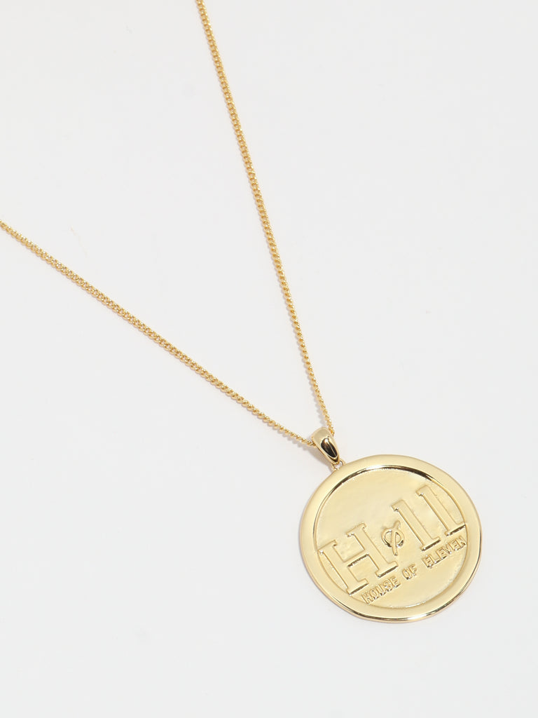 gold necklace with circle shaped pendant with House of eleven logo printed in the center