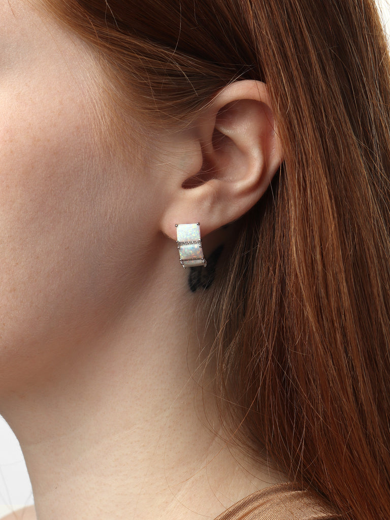 woman wearing silver stud earrings with 3 square shaped opal gems and two columns of clear-colored crystals in between them