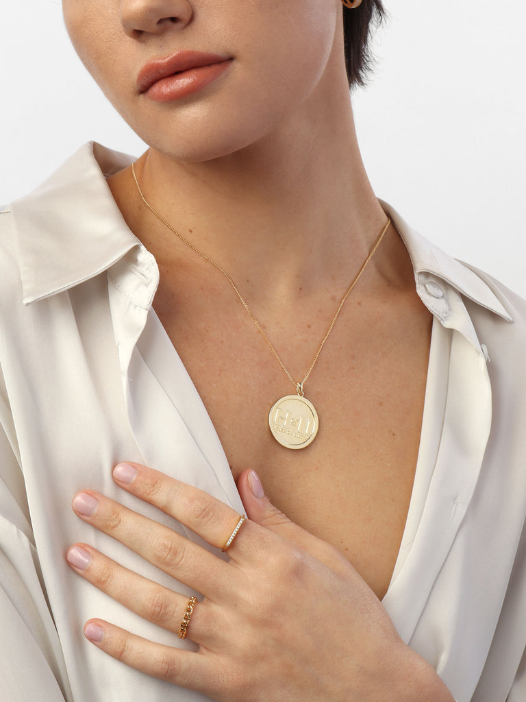 woman wearing gold necklace with circle shaped pendant with House of eleven logo printed in the center