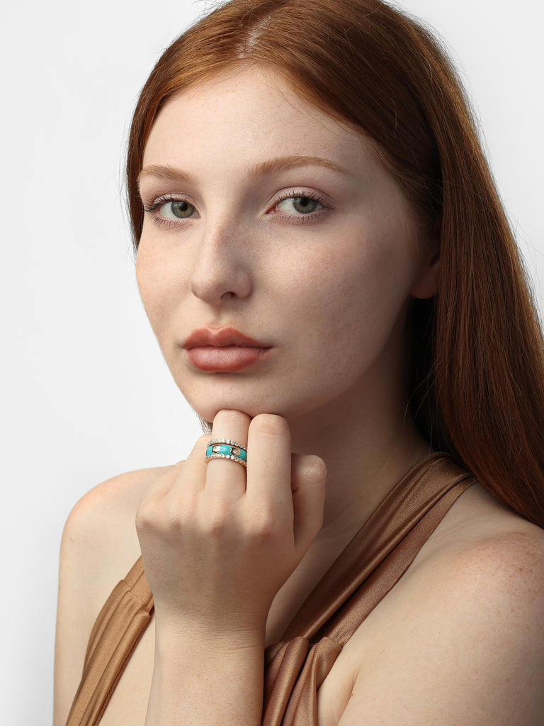 woman wearing three gold rings; two are identically covered in small clear-colored round crystals. the other band is coated with a turquoise enamel with gold flower shaped motif with a small clear-colored crystal in the center