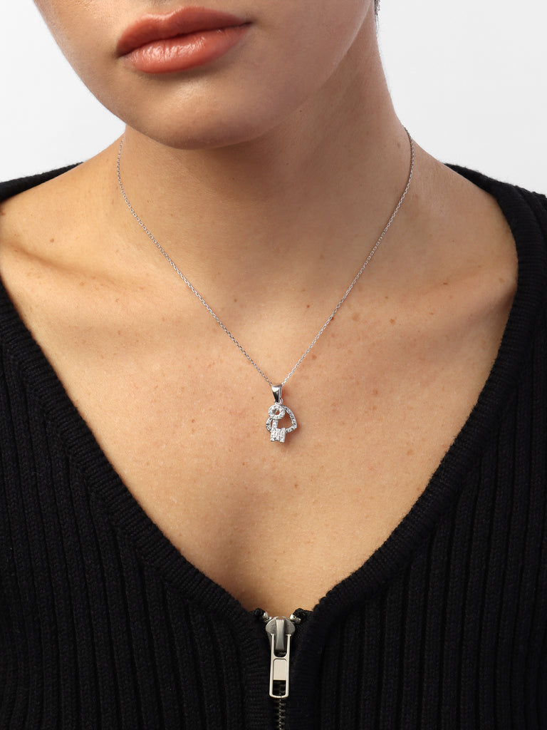 woman wearing silver necklace with two pendants covered in clear-colored crystals in the shape of a heart and key