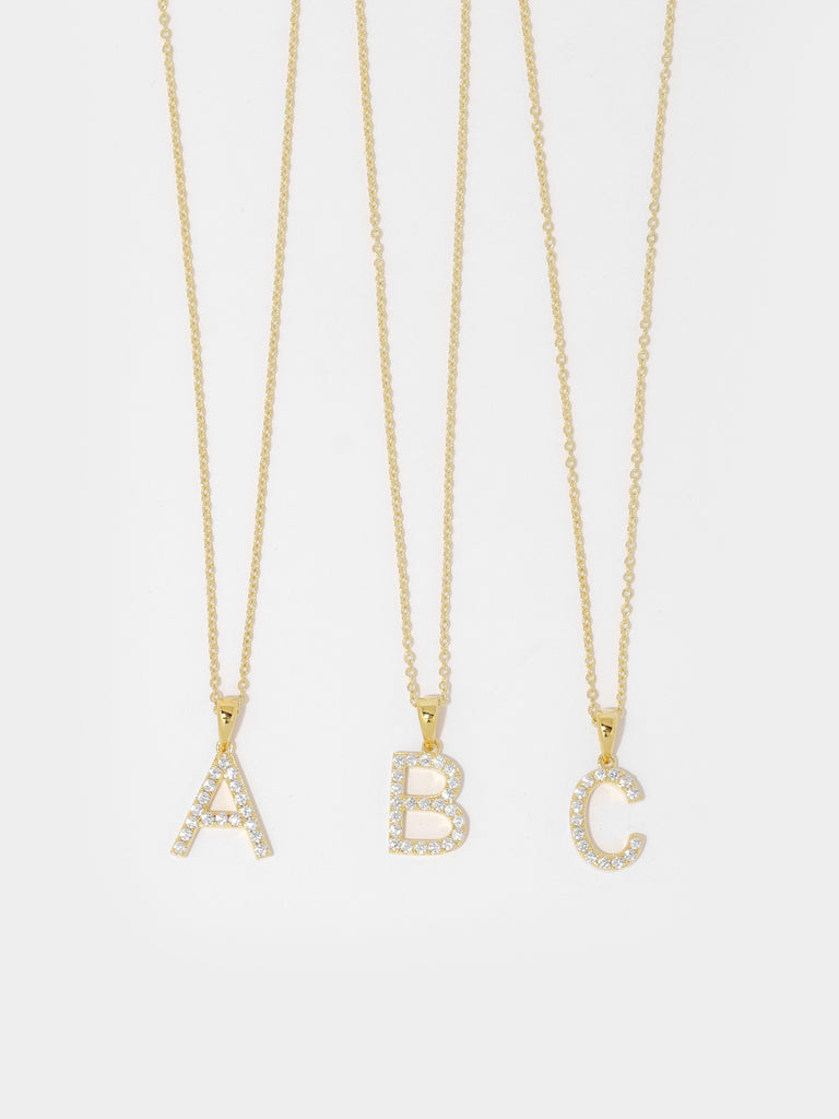 gold necklace with pendants in the shape of letters; A, B, and C. The pendants are covered in clear-colored round crystal gems