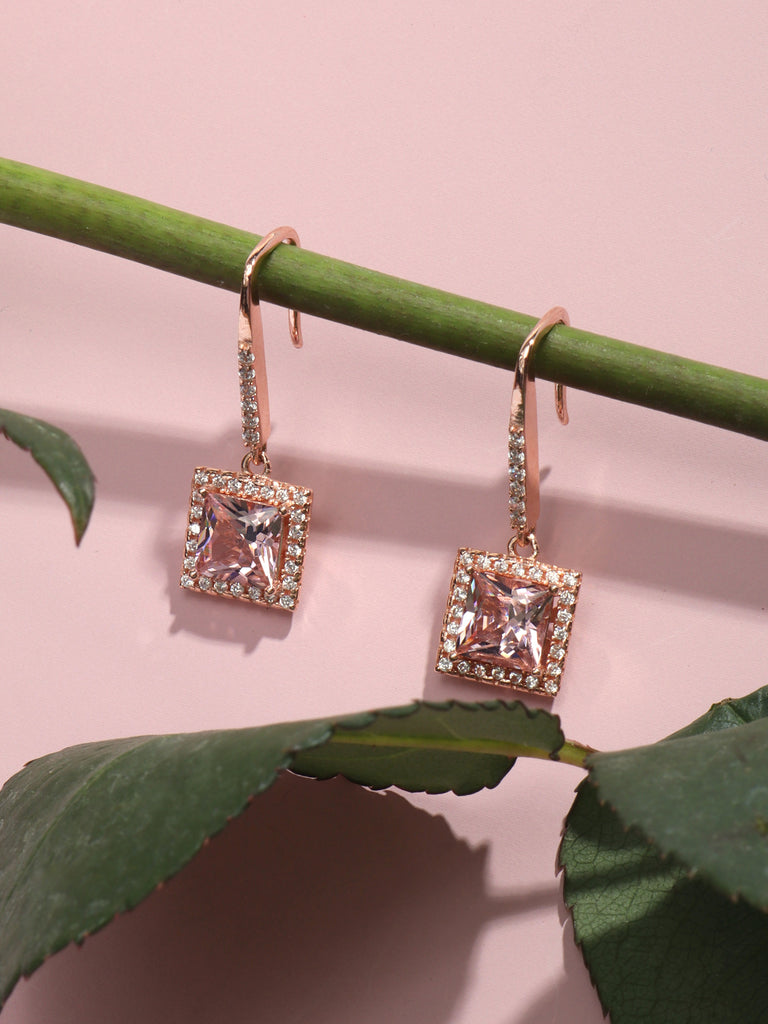 rose gold dangle hook earrings with large square, pink gem surrounded by small clear-colored crystal gems hanging on plant stem